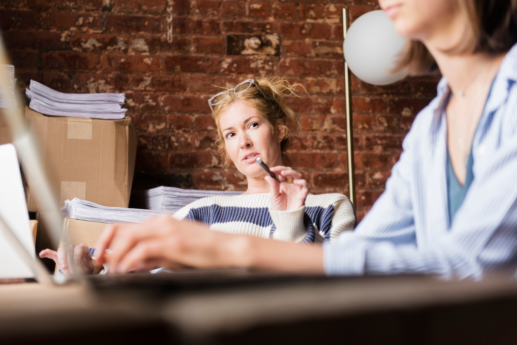 Woman discussing strategy with co-workers, pointing with pen at desk in modern office